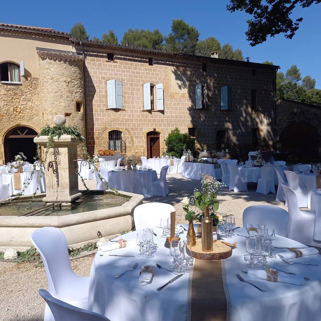 Tables de mariage dressées devant la fontaine et les bâtiments en pierre du domaine